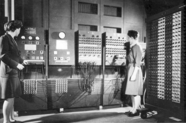 Två kvinnor arbetar vid ENIAC:s huvudkontrollpanel och ställer in reglage på maskinens frontpaneler.